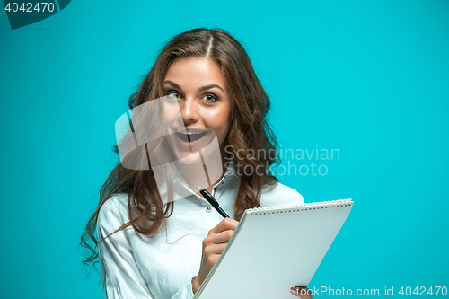 Image of Surprised young business woman with pen and tablet for notes on blue background