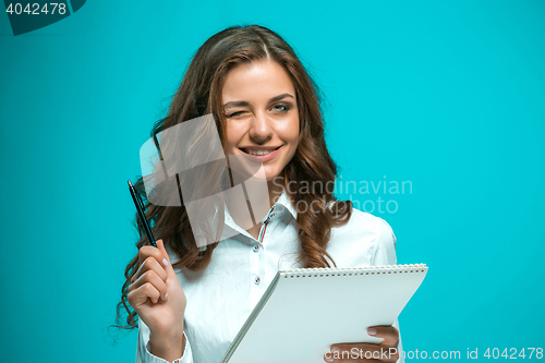 Image of The smiling young business woman with pen and tablet for notes on blue background