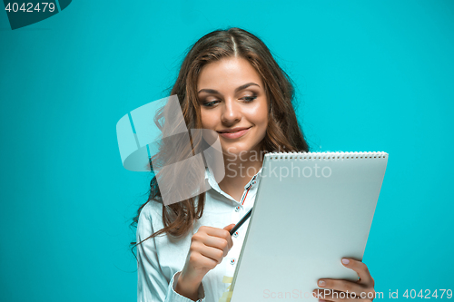 Image of The smiling young business woman with pen and tablet for notes on blue background