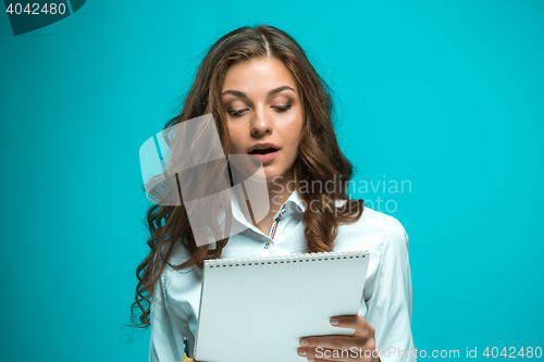 Image of Surprised young business woman with pen and tablet for notes on blue background