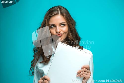 Image of The displeased young business woman with pen and tablet for notes on blue background