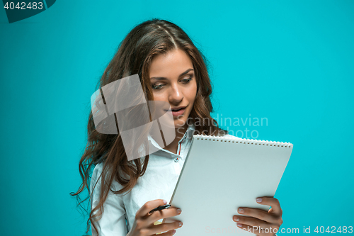 Image of The smiling young business woman with pen and tablet for notes on blue background