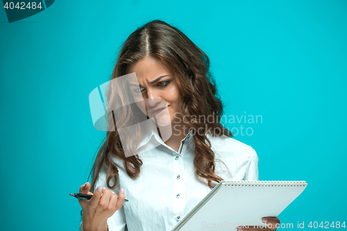 Image of The displeased young business woman with pen and tablet for notes on blue background