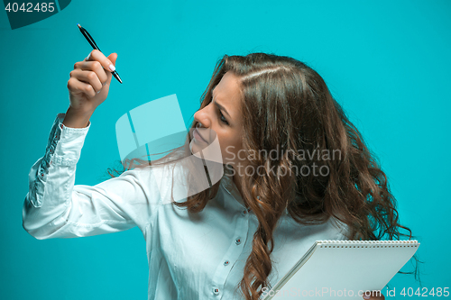 Image of The displeased young business woman with pen and tablet for notes on blue background