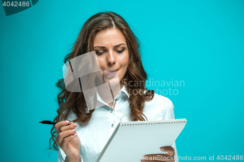 Image of The displeased young business woman with pen and tablet for notes on blue background