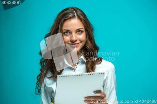 Image of The smiling young business woman with pen and tablet for notes on blue background
