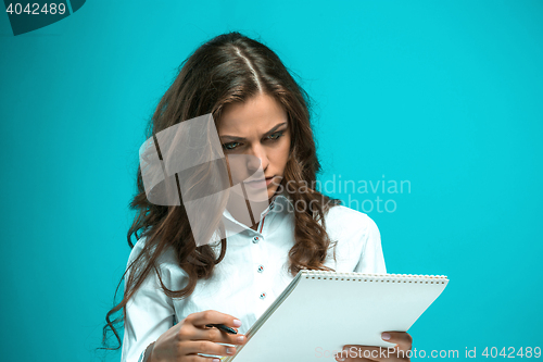 Image of The displeased young business woman with pen and tablet for notes on blue background