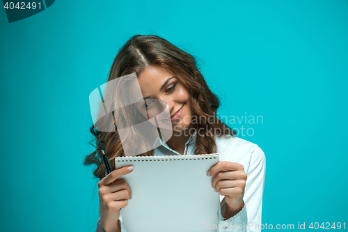 Image of The smiling young business woman with pen and tablet for notes on blue background