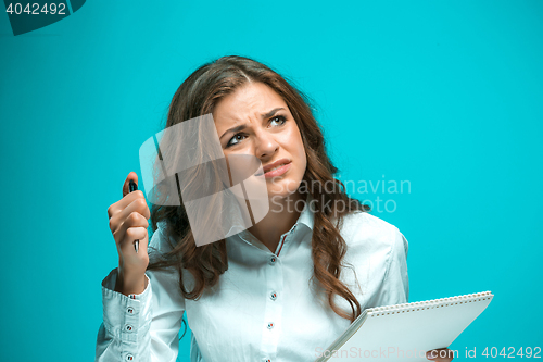 Image of The displeased young business woman with pen and tablet for notes on blue background