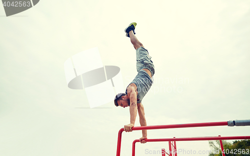 Image of young man exercising on parallel bars outdoors