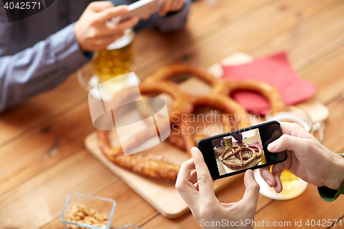 Image of close up of hands picturing pretzel by smartphone