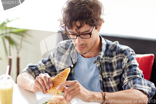Image of happy man eating sandwich at cafe for lunch