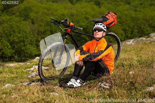 Image of Young man sitting near the cycle on a green meadow