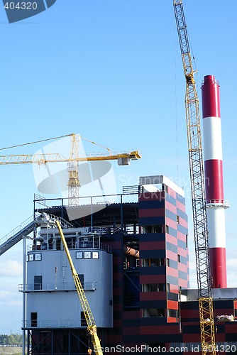 Image of cranes and chinmey on construction of industrial factory