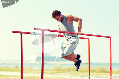 Image of young man exercising on parallel bars outdoors