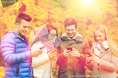 Image of smiling friends with smartphones in city park