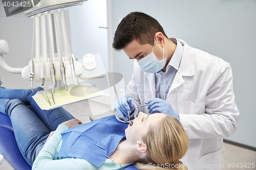 Image of male dentist in mask checking female patient teeth