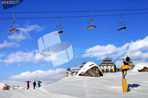 Image of Chair-lift in blue sky and three skiers on ski slope at sun nice