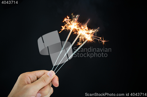 Image of hand holding sparklers over black background