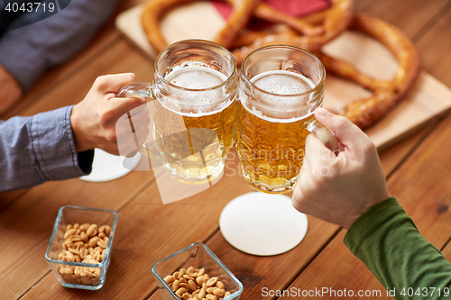 Image of close up of hands clinking beer mugs at bar or pub