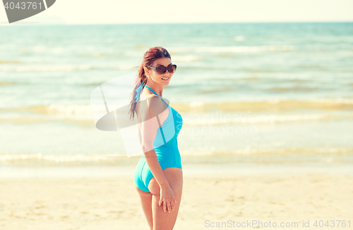 Image of young woman in swimsuit walking on beach