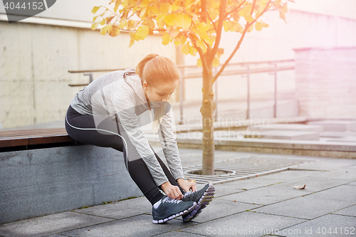 Image of happy young sporty woman tying shoelaces outdoors