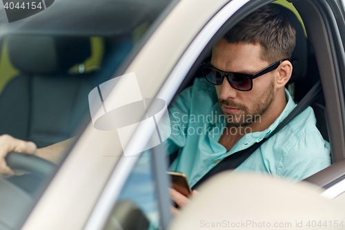 Image of man in sunglasses driving car with smartphone