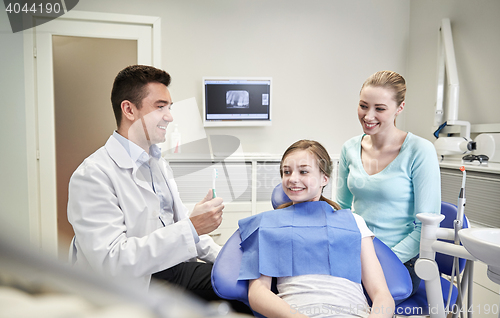 Image of happy dentist showing toothbrush to patient girl