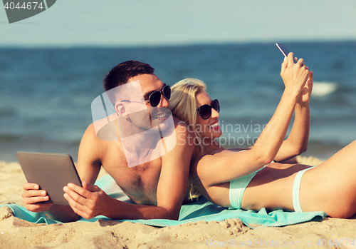 Image of happy couple with modern gadgets lying on beach