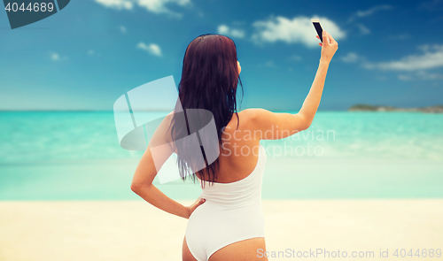 Image of young woman taking selfie with smartphone on beach