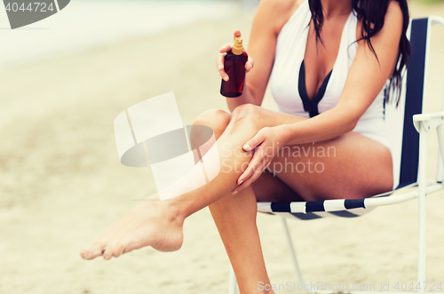 Image of woman spraying sunscreen oil to her skin on beach