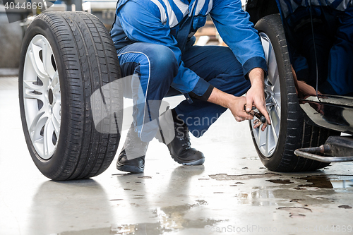 Image of Male Mechanic Changing Car Tire In Garage