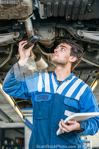 Image of Mechanic Holding Flashlight While Examining Car Exhaust System