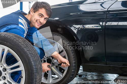 Image of Confident Mechanic Changing Car Tire At Automobile Shop