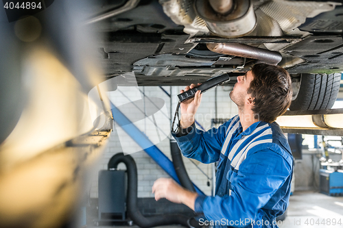 Image of Mechanic With Flashlight Examining Under The Car