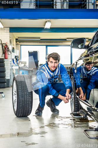 Image of Mechanic Crouching While Changing Car Tire At Garage