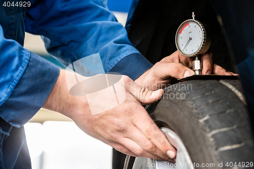 Image of Hands Of Mechanic Pressing Gauge Into Tire In Garage