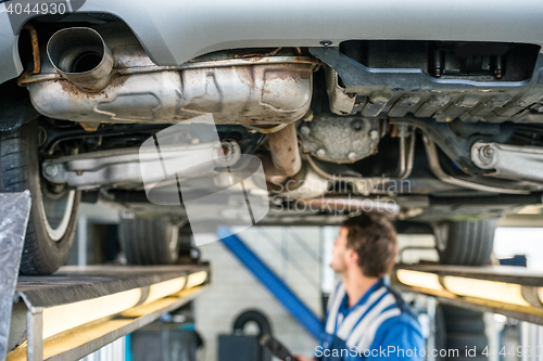 Image of Car On Hydraulic Lift With Mechanic Working In Garage