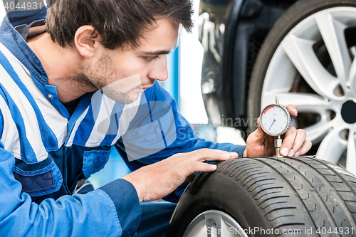 Image of Young Male Mechanic Pressing Gauge Into Tire In Garage