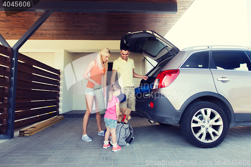 Image of happy family packing things to car at home parking