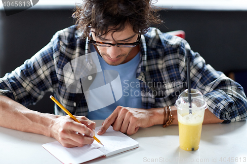 Image of man with notebook and juice writing at cafe