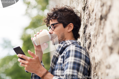 Image of man with smartphone drinking coffee on city street