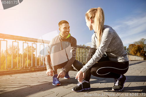 Image of smiling couple tying shoelaces outdoors