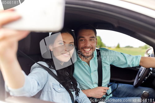 Image of happy couple in car taking selfie with smartphone