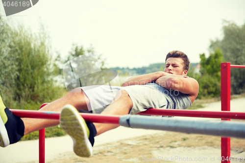 Image of young man doing sit up on parallel bars outdoors