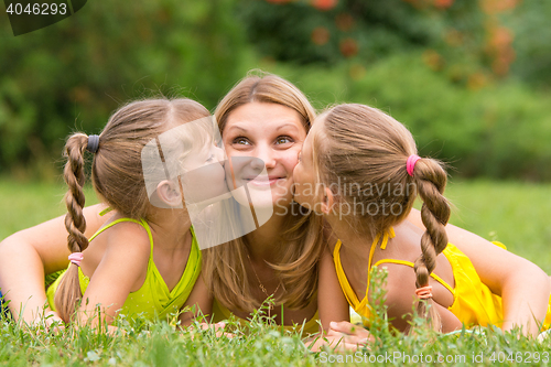 Image of Two daughters kissing mother lying on the grass on a picnic, Mother looked up fun