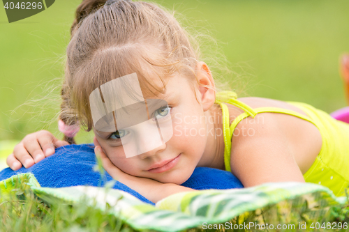 Image of Five-year girl lies on a bed on a green meadow and touching looking to the frame