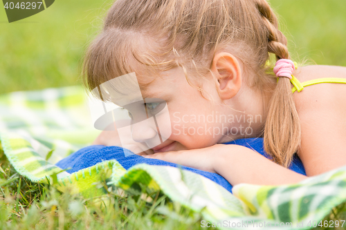 Image of Five-year girl lies on a green meadow and touching looking at grass