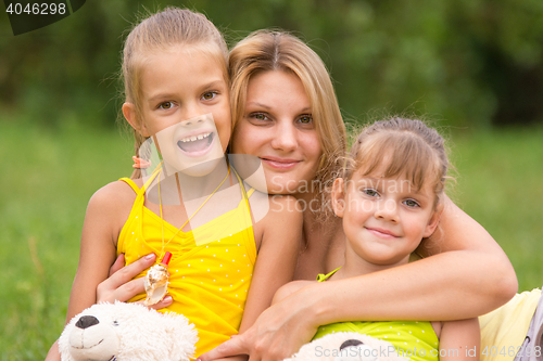 Image of Young mother hugging her two daughters, five and seven years