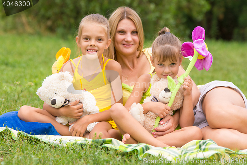 Image of Young mother sitting on a picnic in a clearing with two daughters